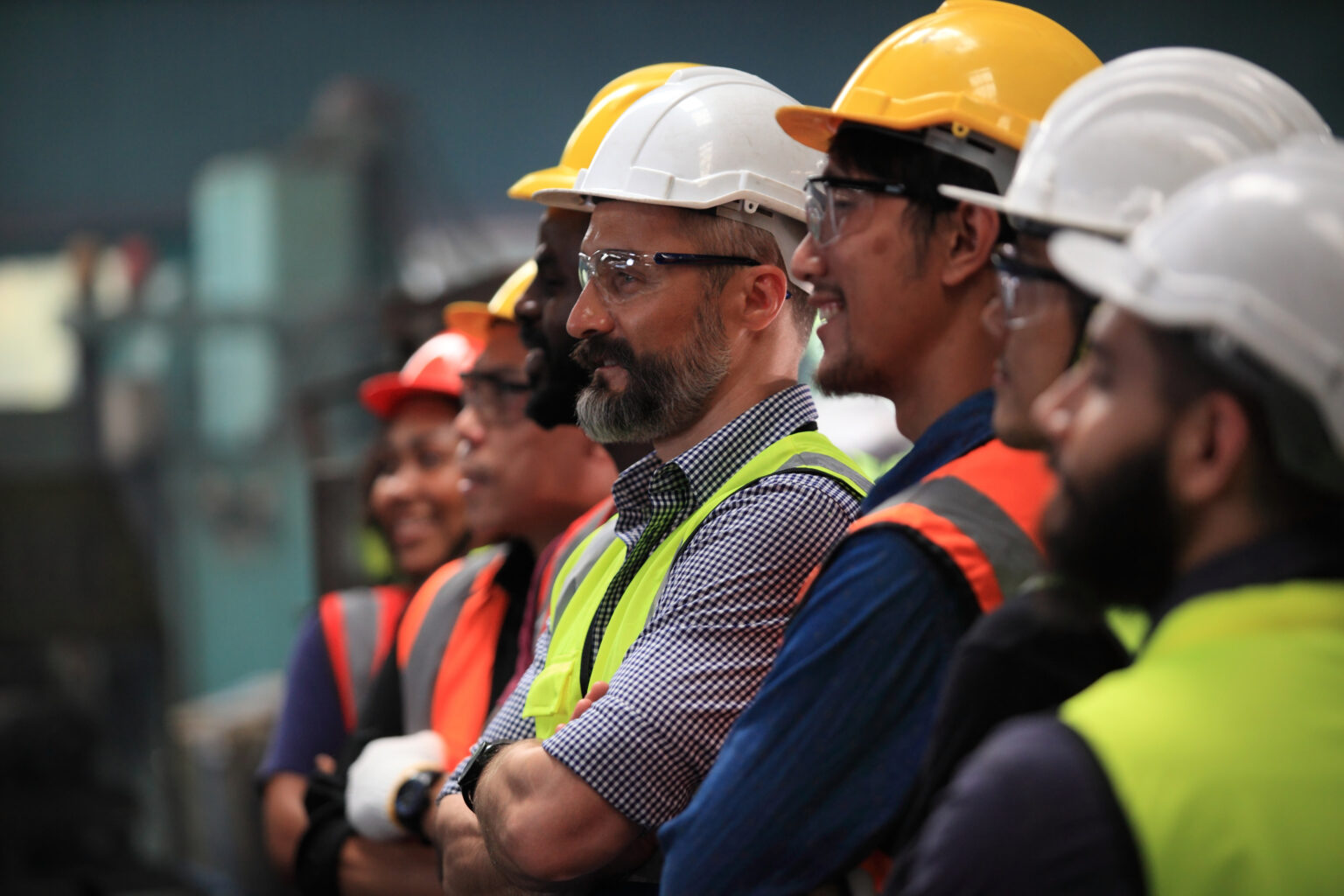 Group of factory workers in hard hats and safety vests standing together on a production floor