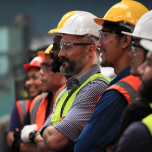 Group of factory workers in hard hats and safety vests standing together on a production floor