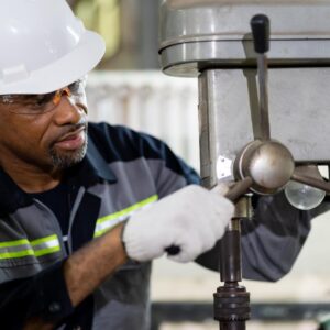 Industrial worker in a hard hat and safety glasses operating a drill press