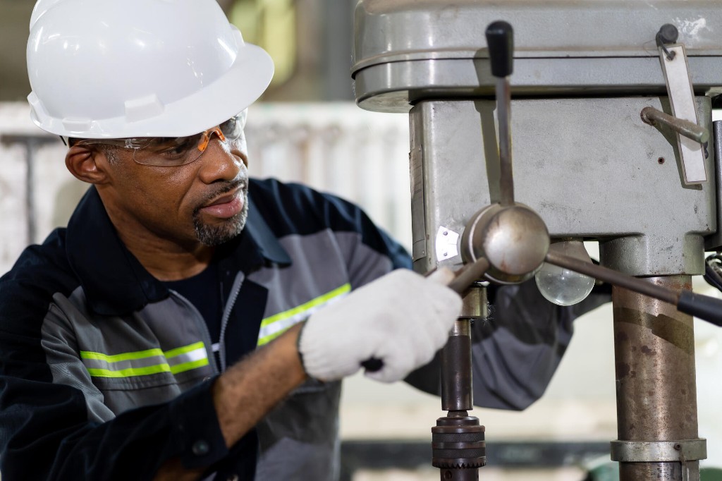 Industrial worker in a hard hat and safety glasses operating a drill press